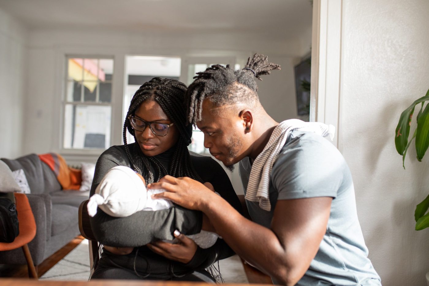 Two new parents at a dining table, both looking down at the newborn one of them is holding.