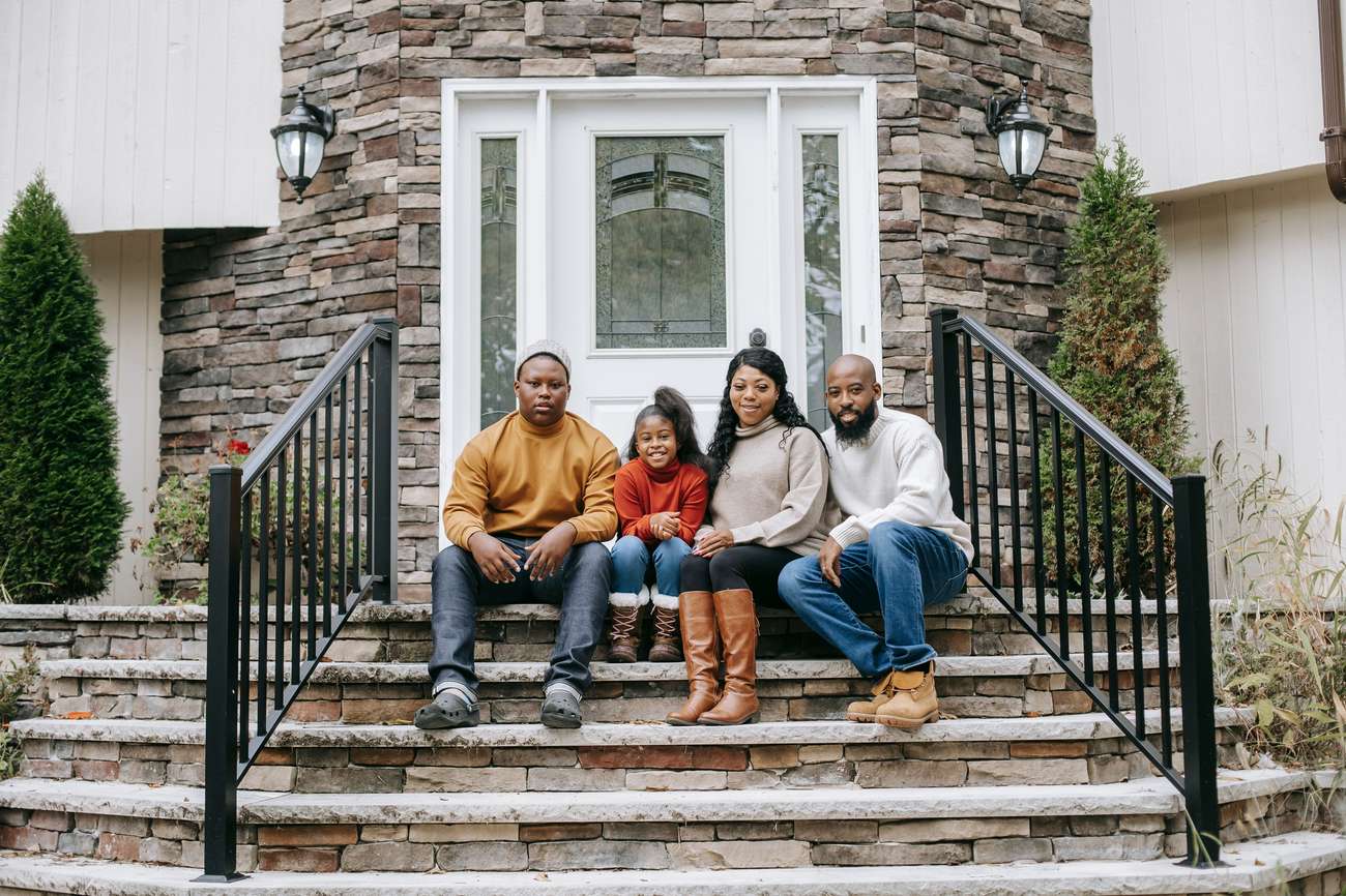 A family of four standing together on the front steps of their home.